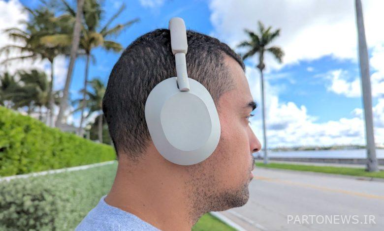 Man Sony WH-1000XM5 wireless headphones outside with blue skies and palm trees in the background