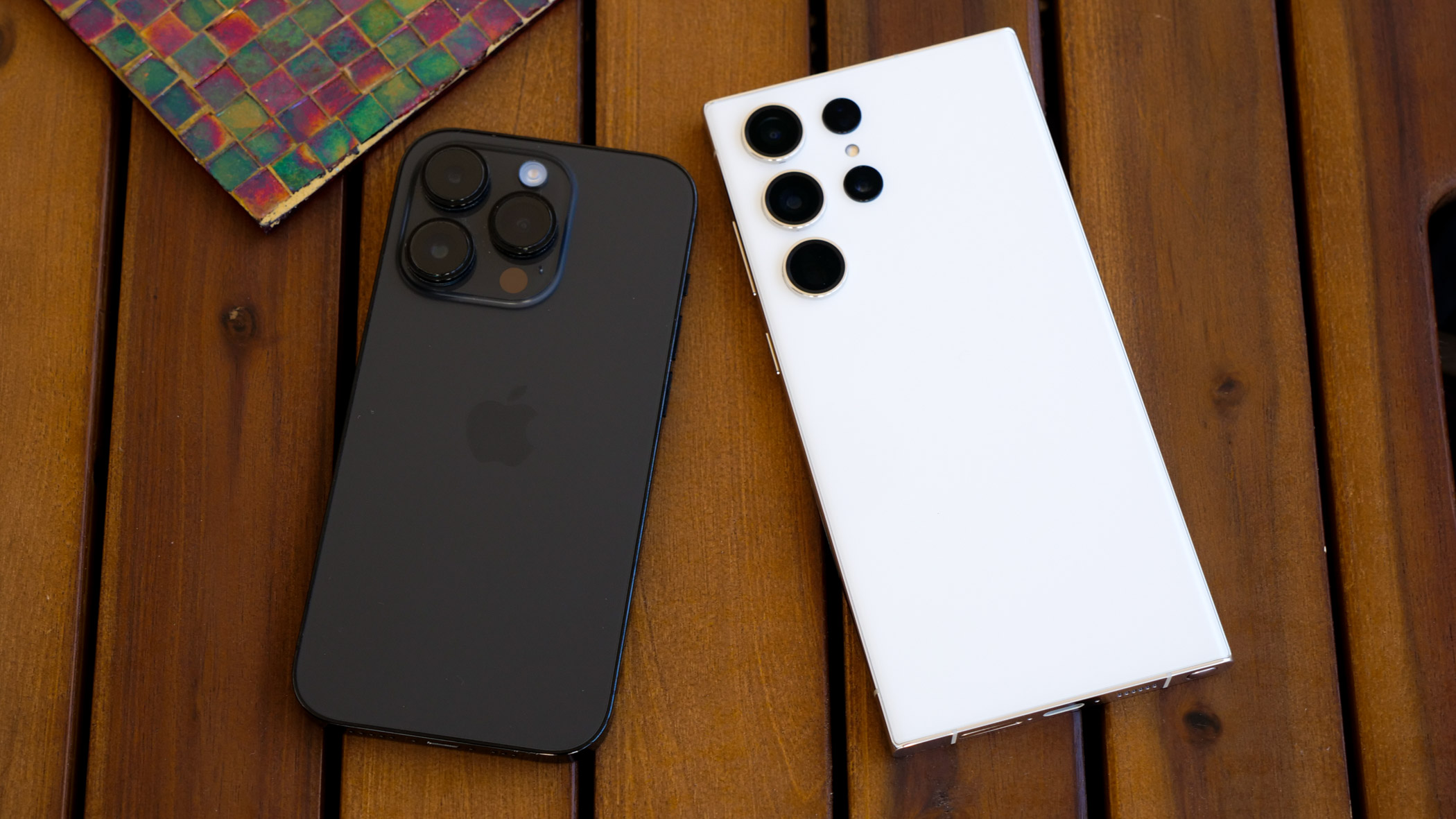 صفحه نمایش iPhone 14 Pro و Galaxy S23 Ultra به سمت پایین روی یک میز کناری چوبی باریک