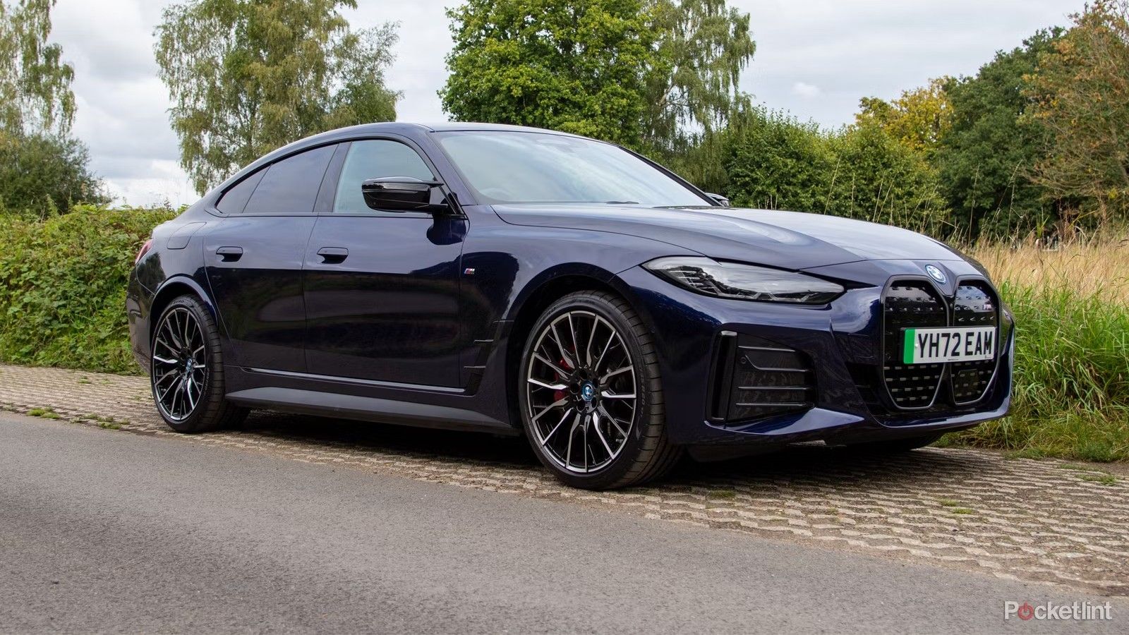 یک BMW i4 EV آبی رنگ در کنار جاده قرار دارد