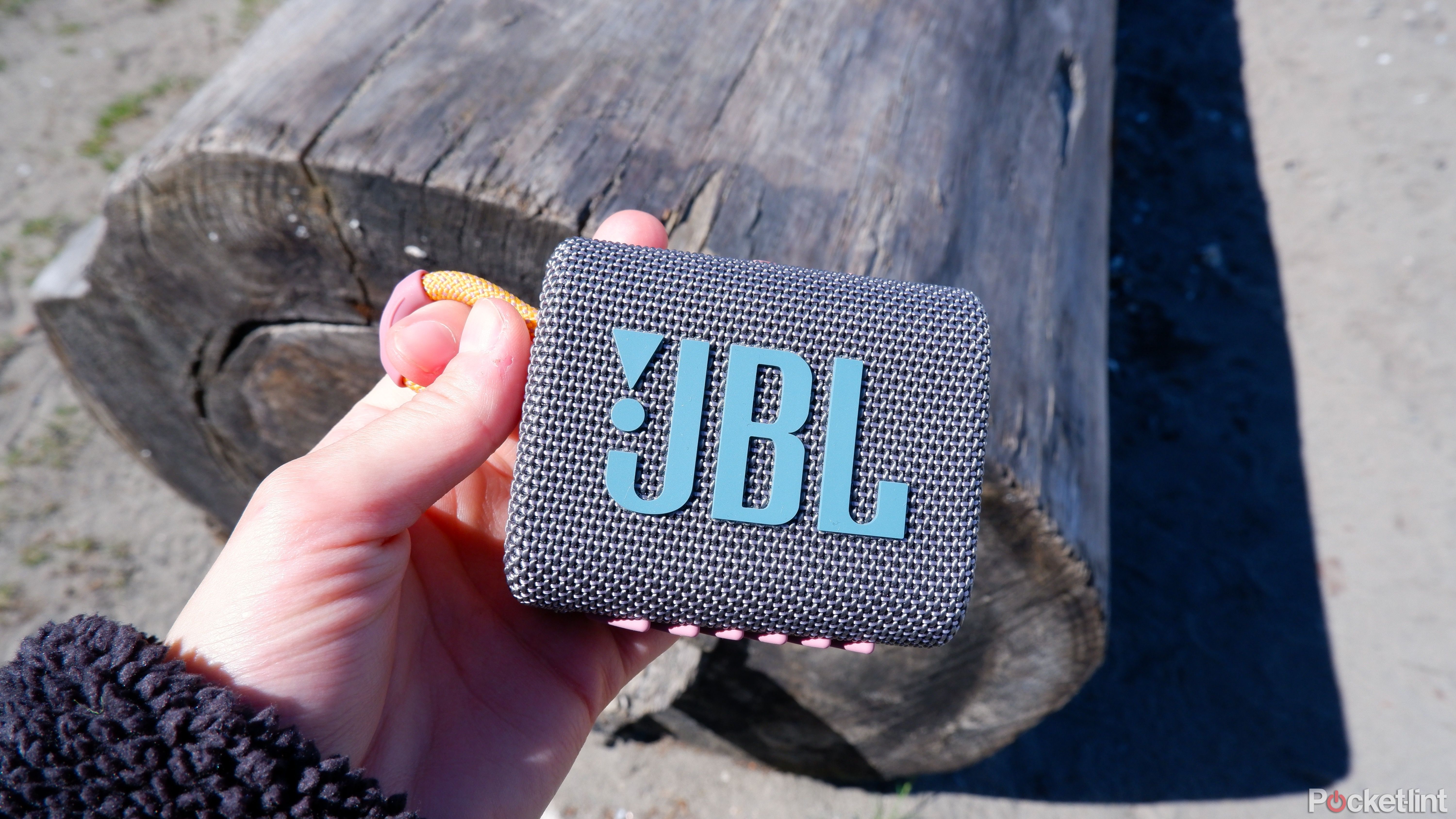 JBL go 3 که در دست در مقابل چوبی در ساحل نگه داشته شده است