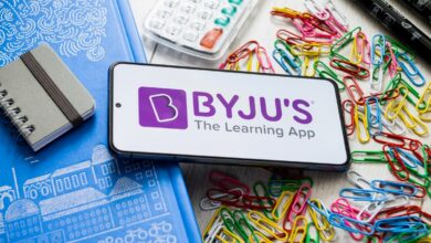 Byju's logo displayed on a smartphone laying on a table covered in school supplies