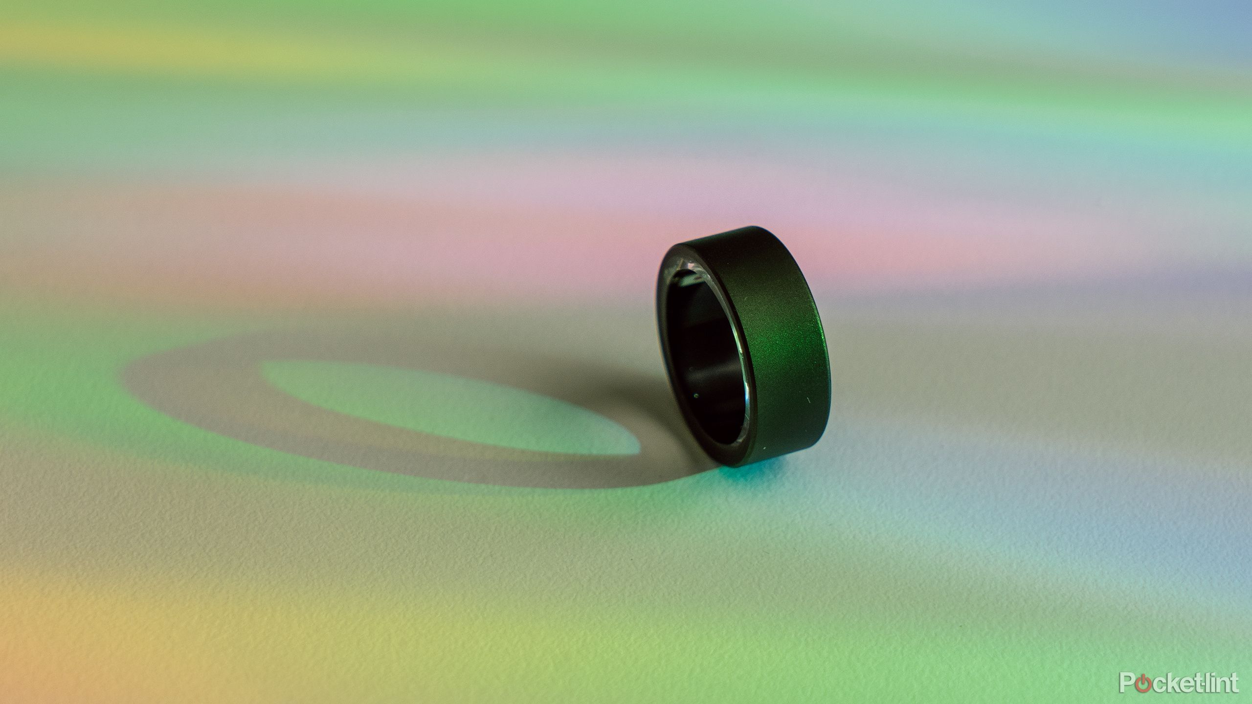 Ultrahuman Ring Air در کنارش روی میز سفیدی با نور رنگین کمان. 
