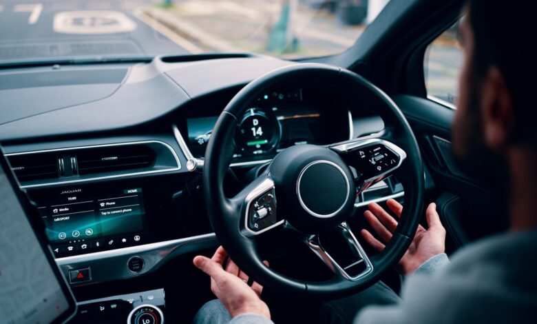 person's hands letting go of steering wheel of self-driving car