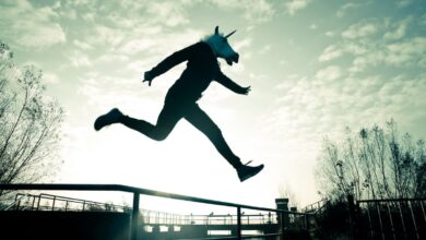 An adult wearing a unicorn mask leaps over a chain-link fence