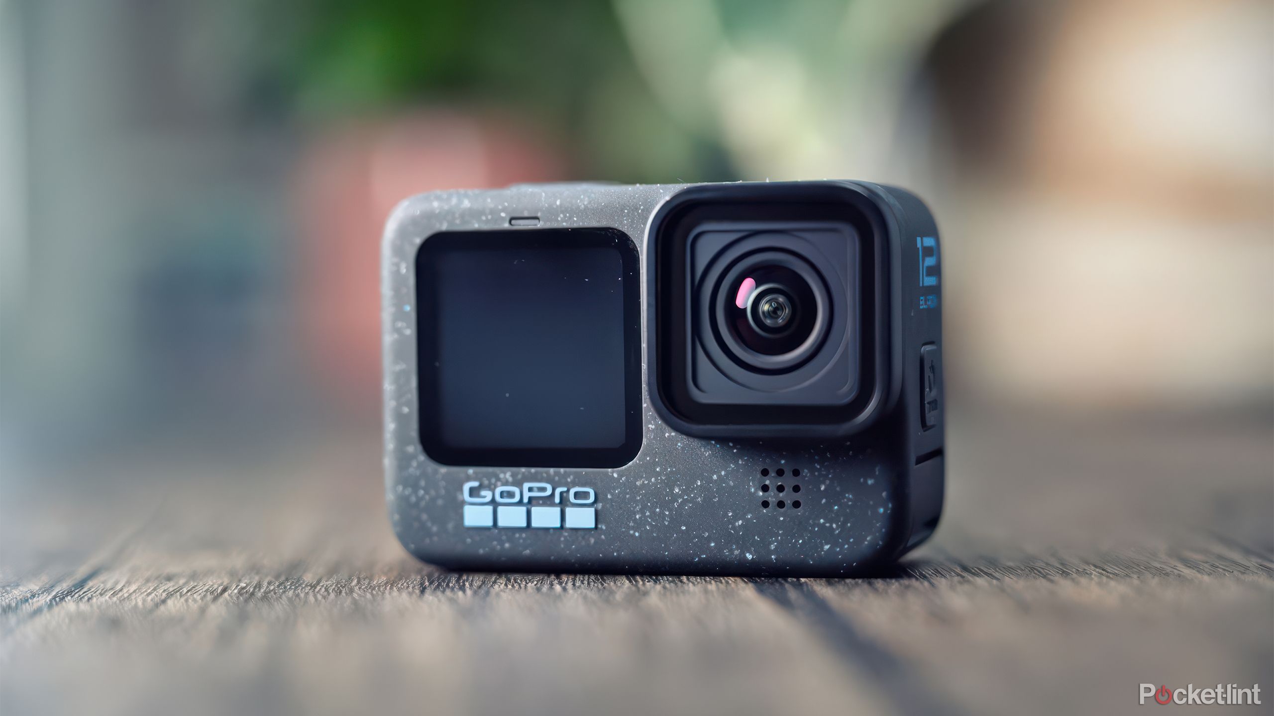 GoPro Hero 12 Black روی یک میز چوبی در مقابل گیاهان تار قرار گرفته است. 