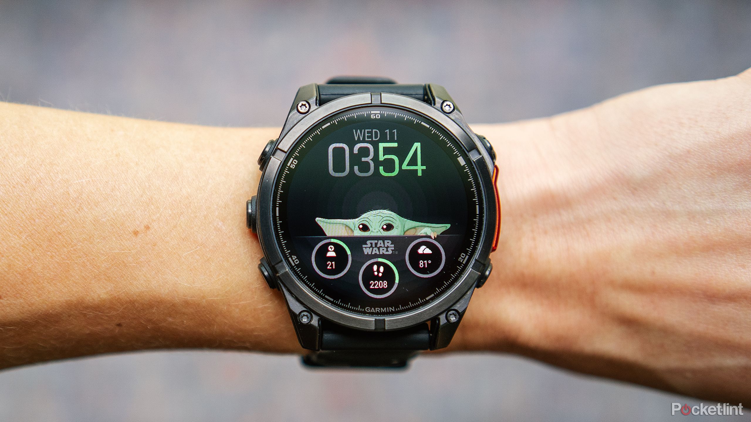Garmin Fenix ​​8 AMOLED با صفحه ساعت Grogu روی مچ دستی بالای پس‌زمینه آبی و قرمز تار قرار دارد. 