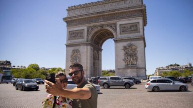 Tourists take selfie pictures in front of the Arc de Triomphe in Paris.