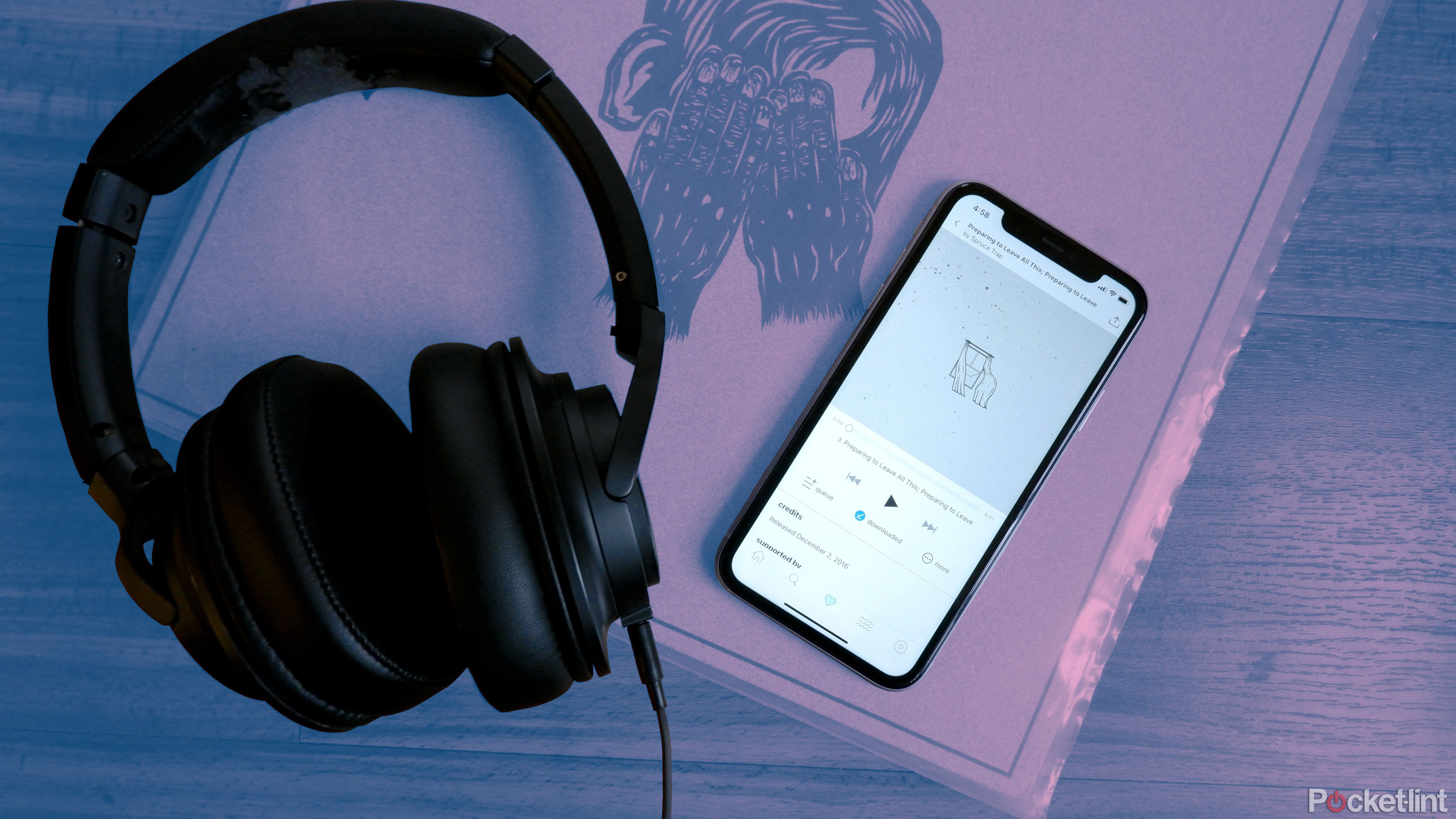 یک جفت هدفون Audio-Technica در کنار تلفنی که آهنگی را از Bandcamp پخش می کند، بالای یک رکورد