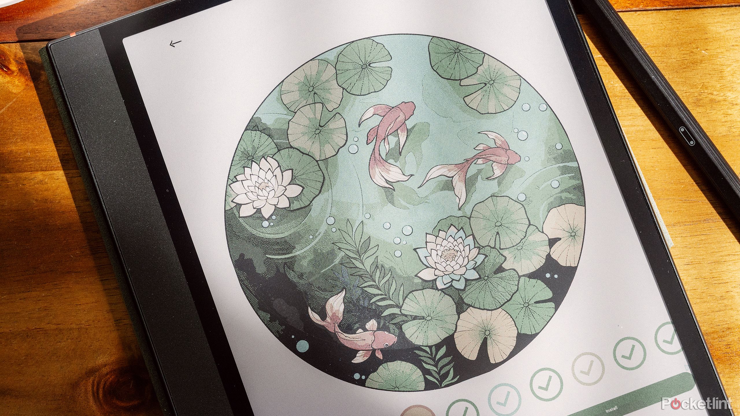 Boox Note Air4 C روی یک میز قهوه چوبی با نقاشی ماهی کوی در یک حوض روی نمایشگر قرار دارد. 