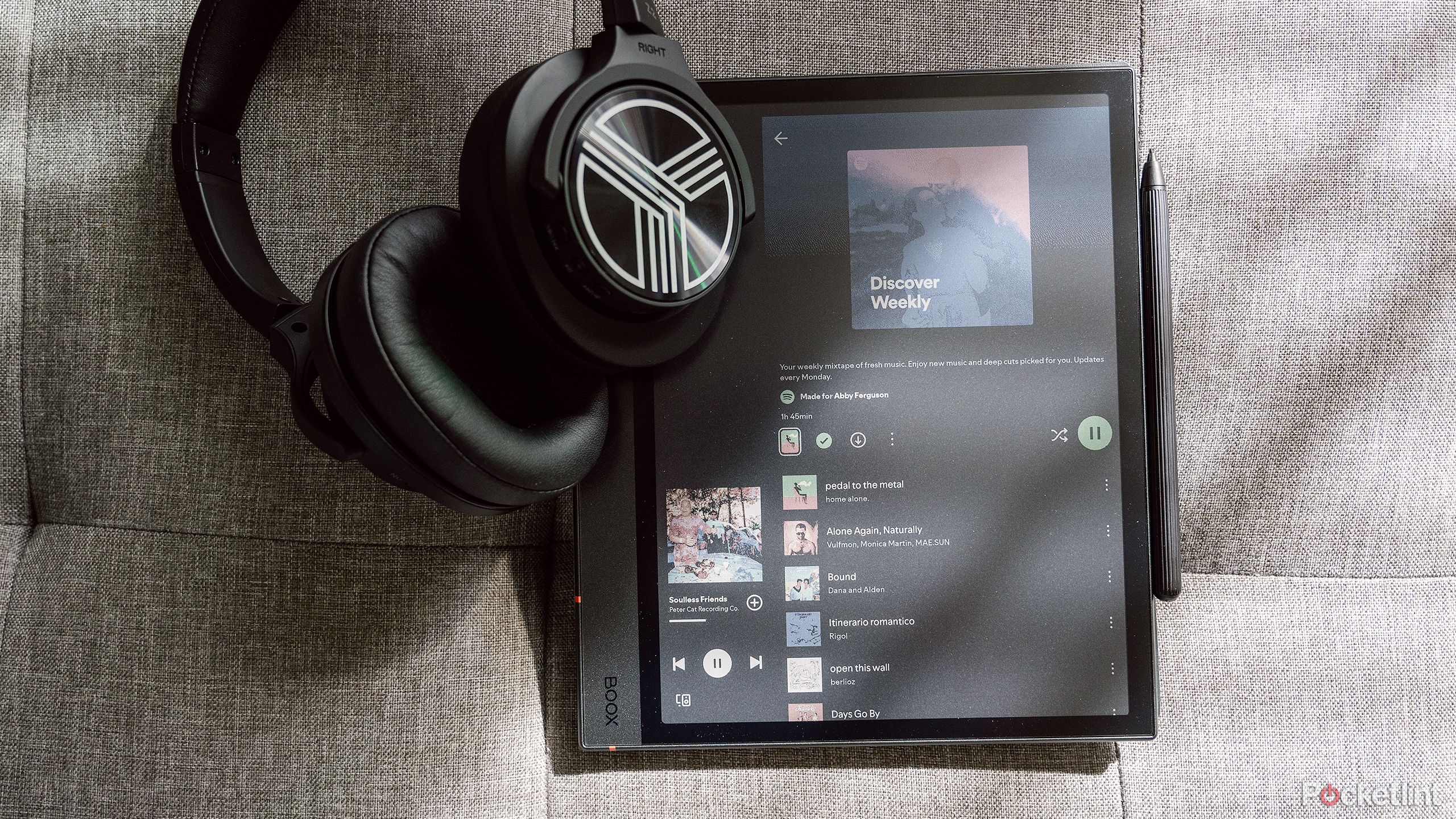 Boox Note Air4 C روی یک کاناپه خاکستری با یک جفت هدفون روی گوش قرار گرفته است. 