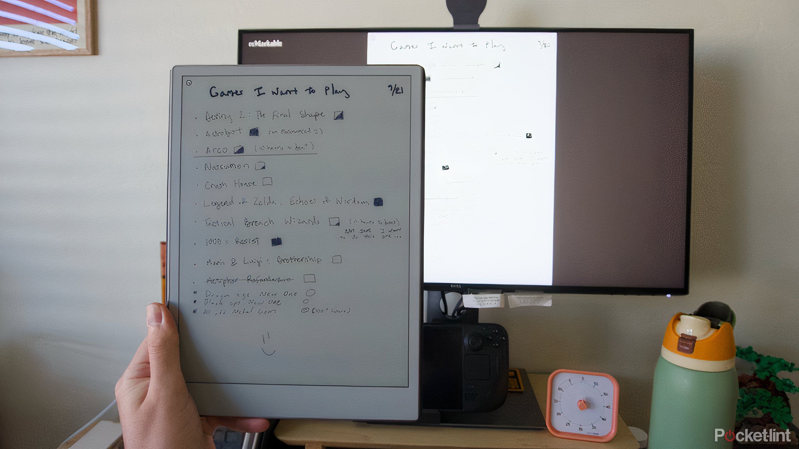 دستی که یک Paper Pro قابل توجه را در دست گرفته و صفحه نمایش را با مانیتور به اشتراک می گذارد.