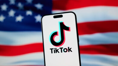 The TikTok app and logo are seen on a mobile device in front of a US flag