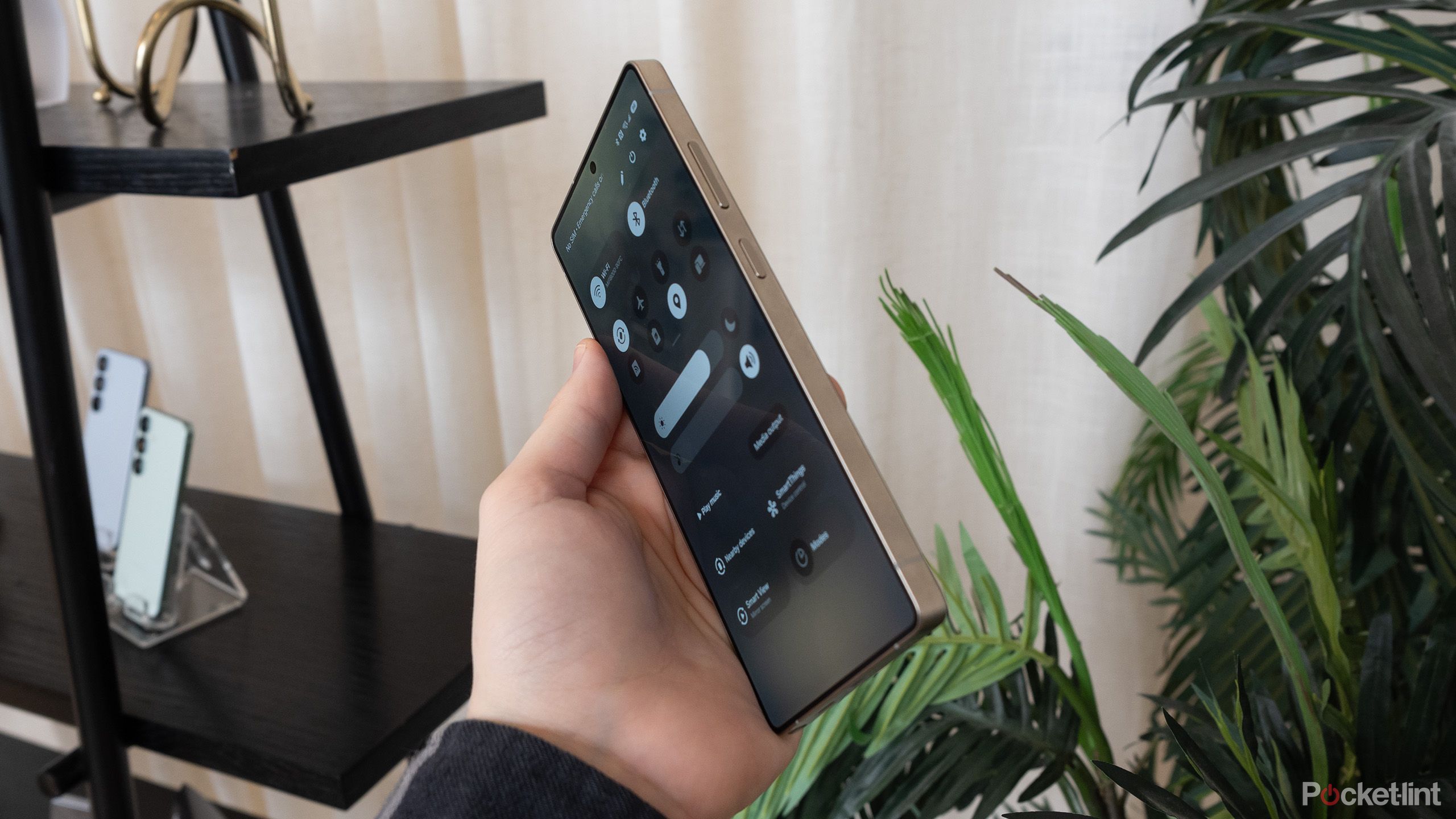 Galaxy S25 Ultra در دست کسی در اتاقی با گیاهان و قفسه‌بندی. 