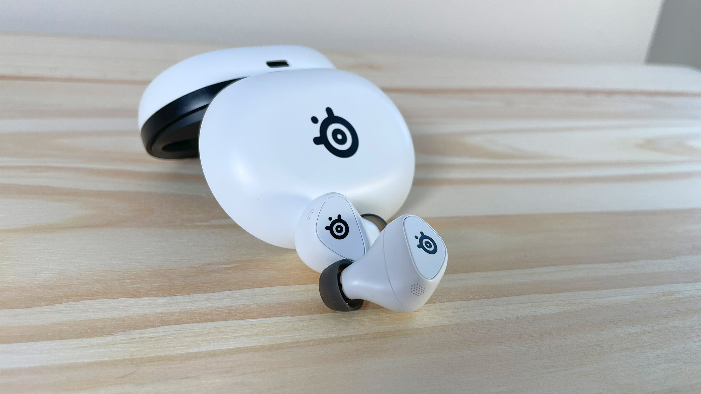 Gamebuds Steelseries Arctis با کیس که روی یک میز چوب قرار گرفته است