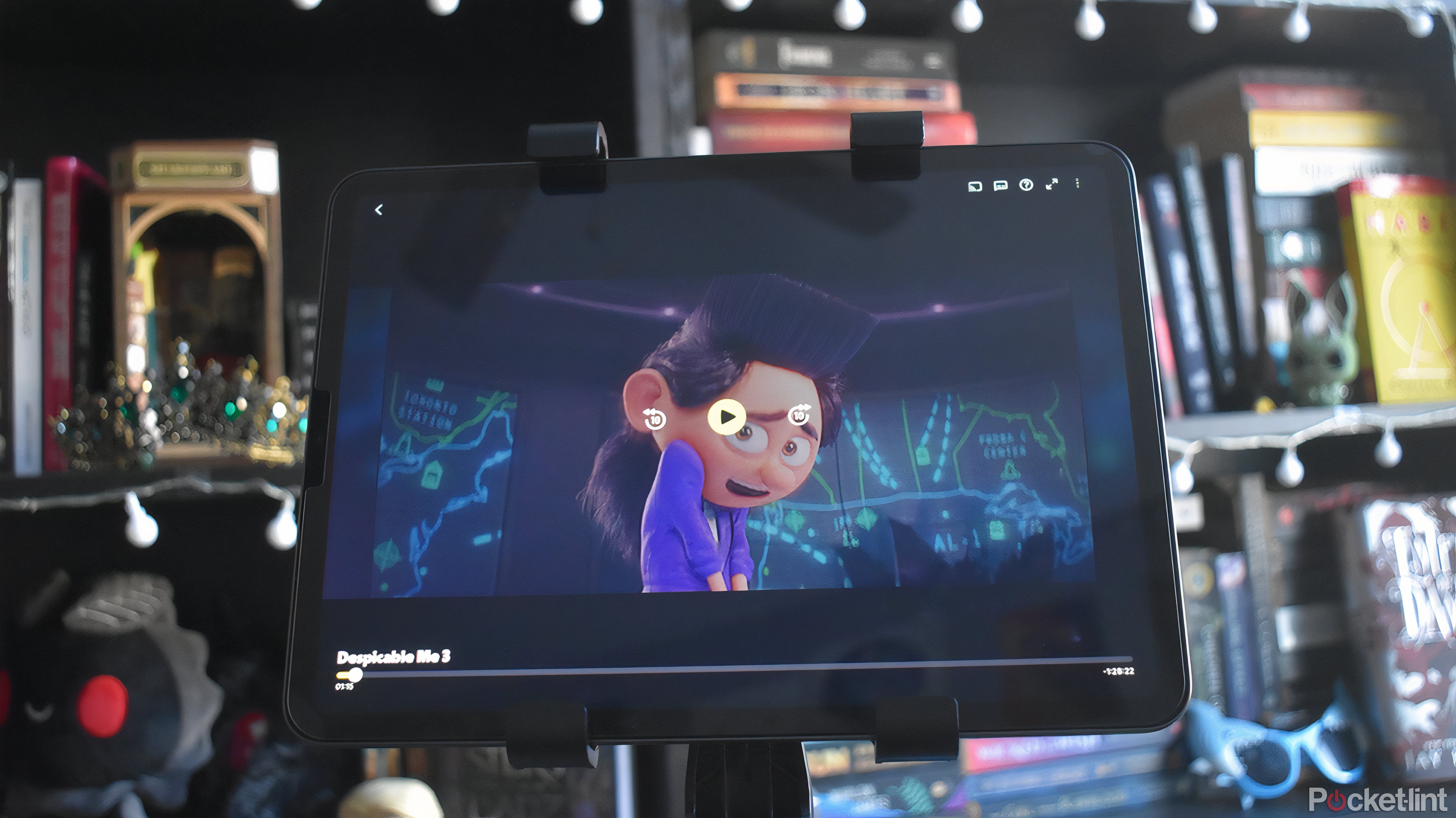 Despicable ME در برنامه Tubi در iPad Pro باز است. دکمه های مکث ، به جلو و عقب نشان داده شده است. در پس زمینه چندین قفسه کتاب وجود دارد.