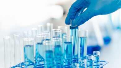 specialty chemicals' testing in a lab; gloved hand picking up one of several vials of blue liquid