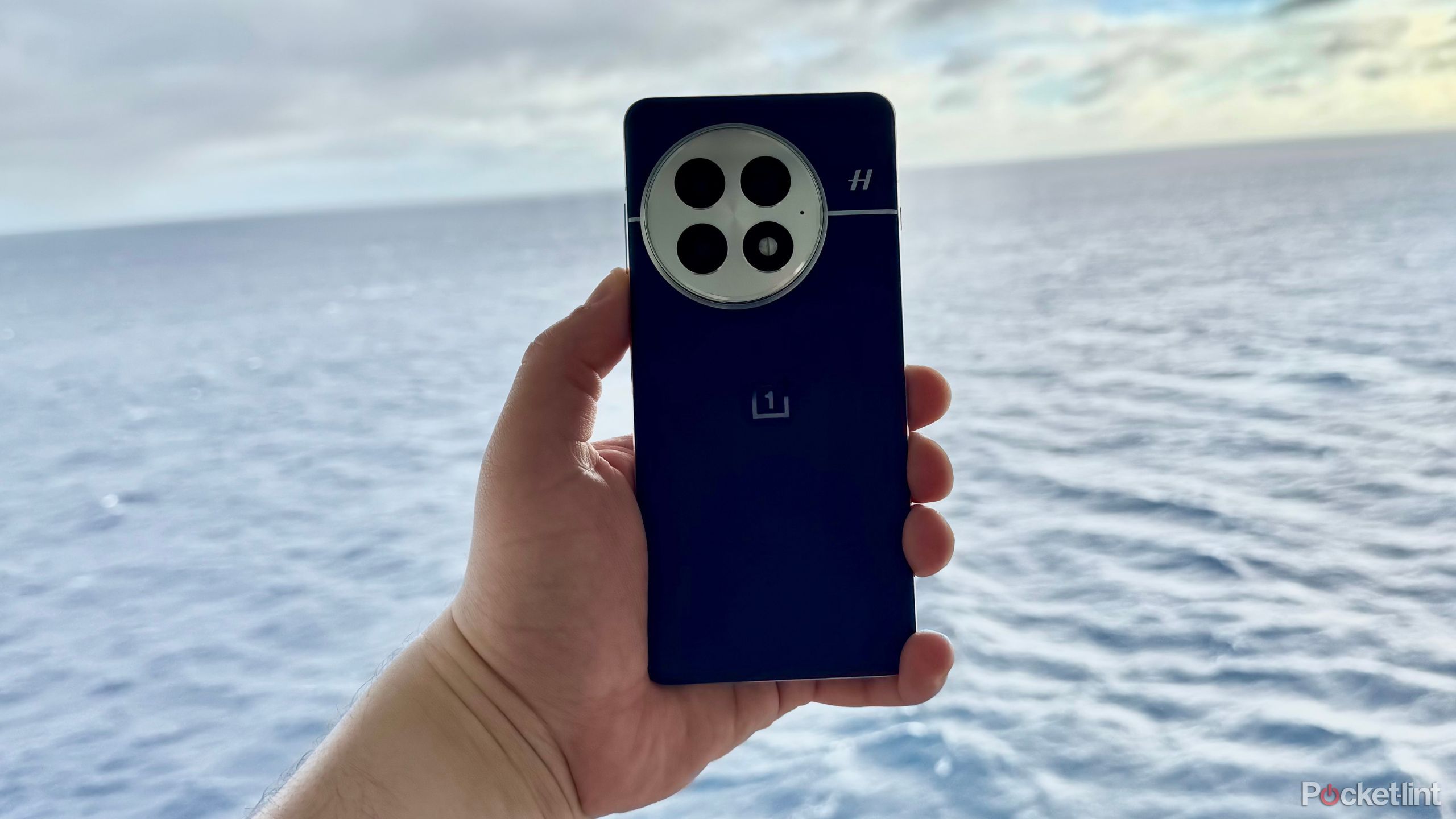 شخصی که OnePlus 13 را بر روی اقیانوس نگه می دارد. 