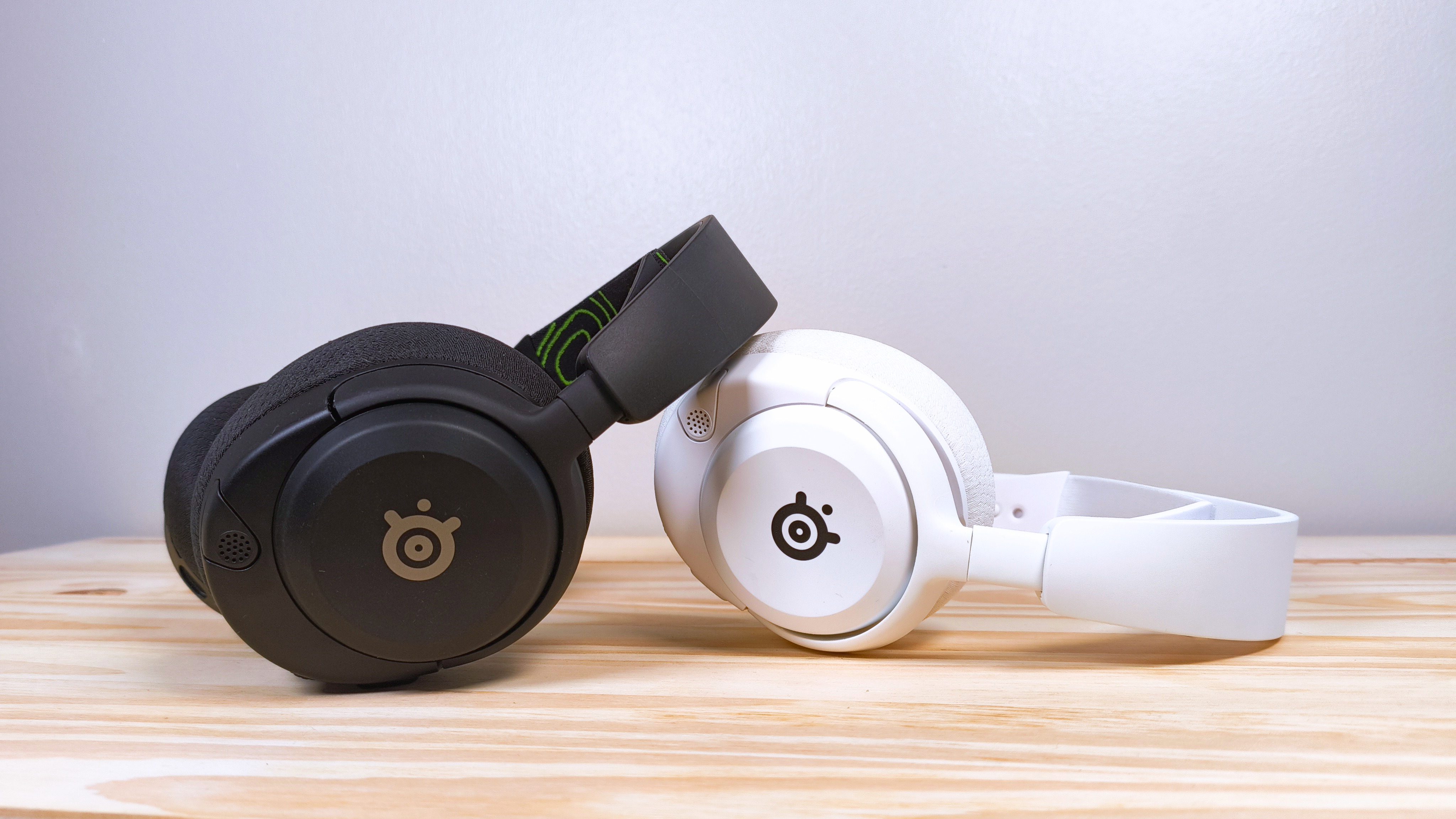 دو جفت از Steelseries Arctis Nova 5x در سیاه و سفید روی یک میز چوبی