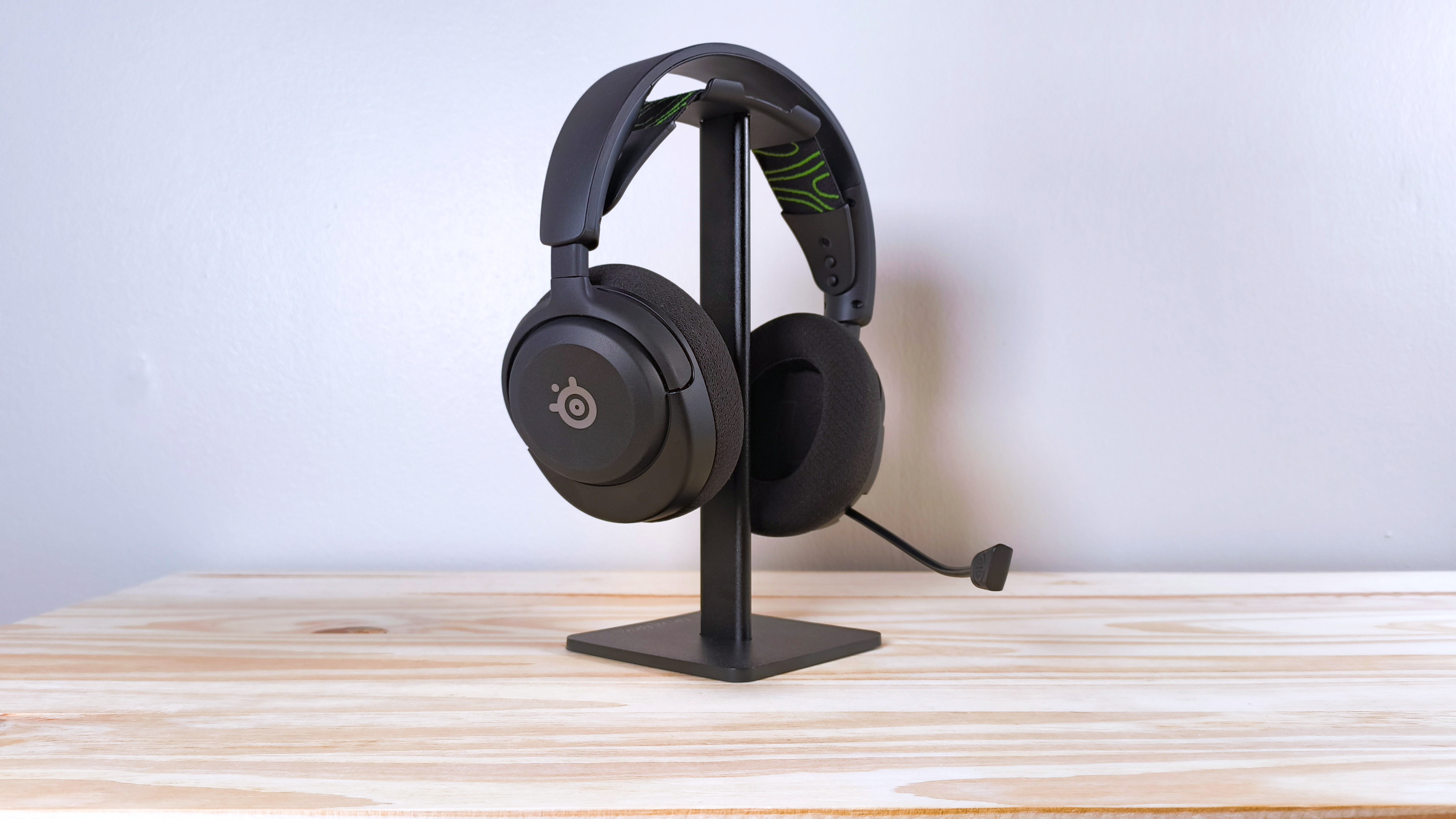 Steelseries Arctis Nova 5x با رنگ مشکی روی یک پایه هدفون روی میز چوب