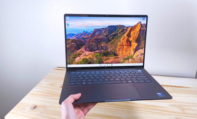 A hand holding up the HP EliteBook Ultra G1i AI with lid open in front of a wood table
