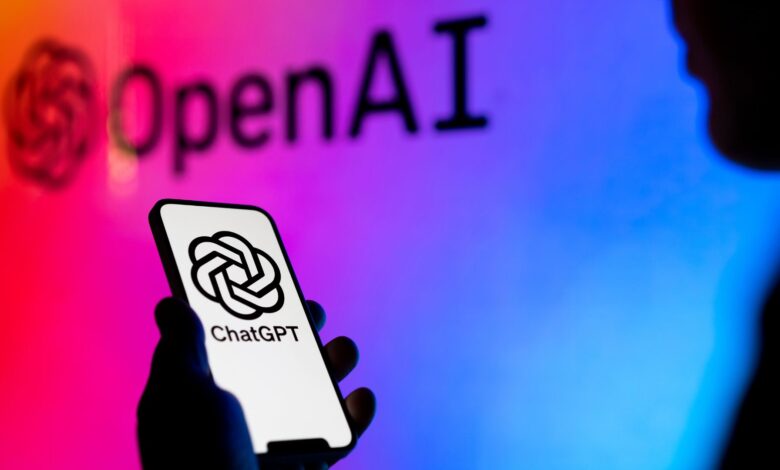 A silhouette of a person holding a phone with the ChatGPT logo on screen in front of an abstract background with the OpenAI logo