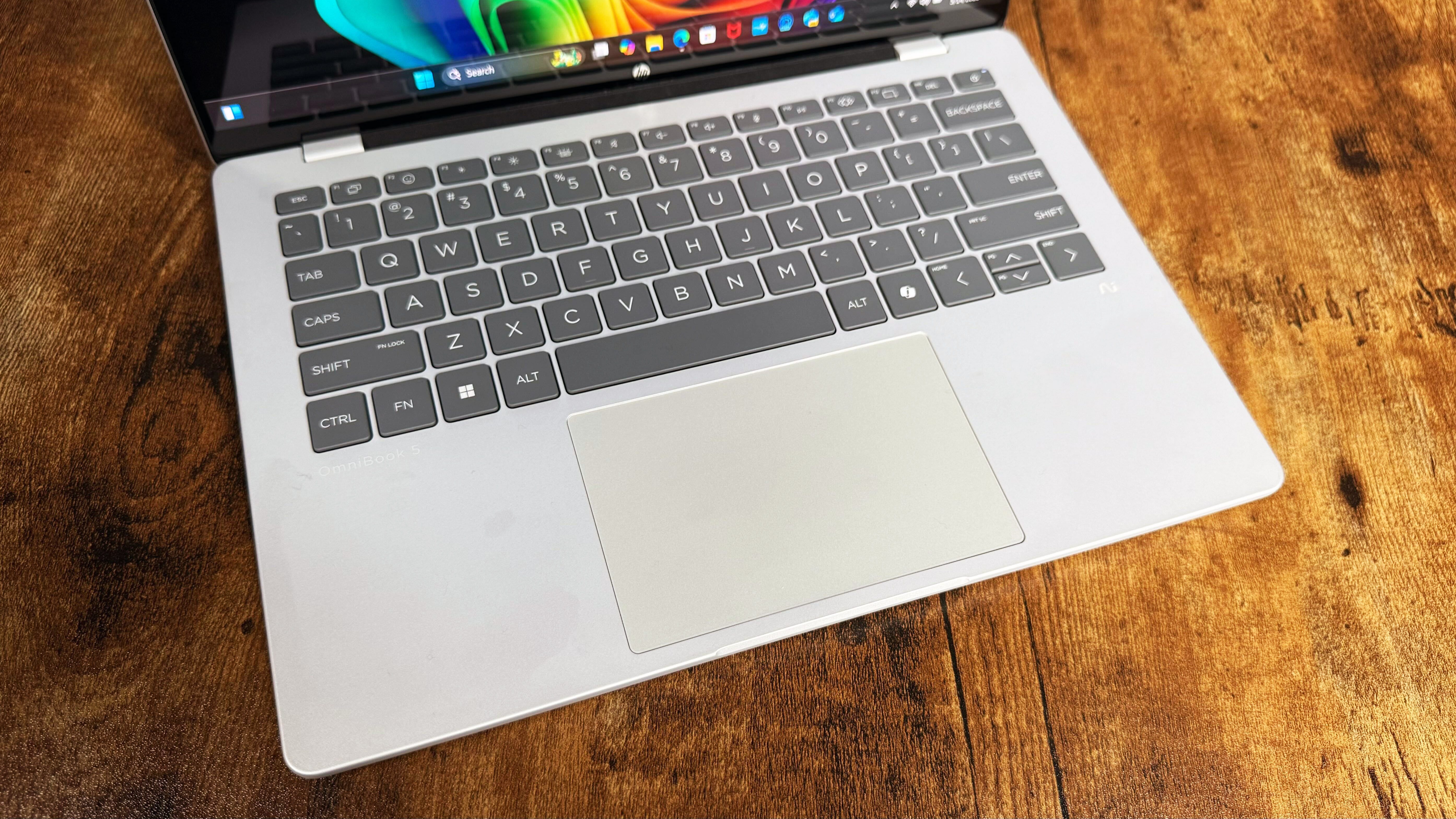 HP Omnibook 5 14 AI PC روی یک میز چوبی در برابر پس زمینه سیاه.