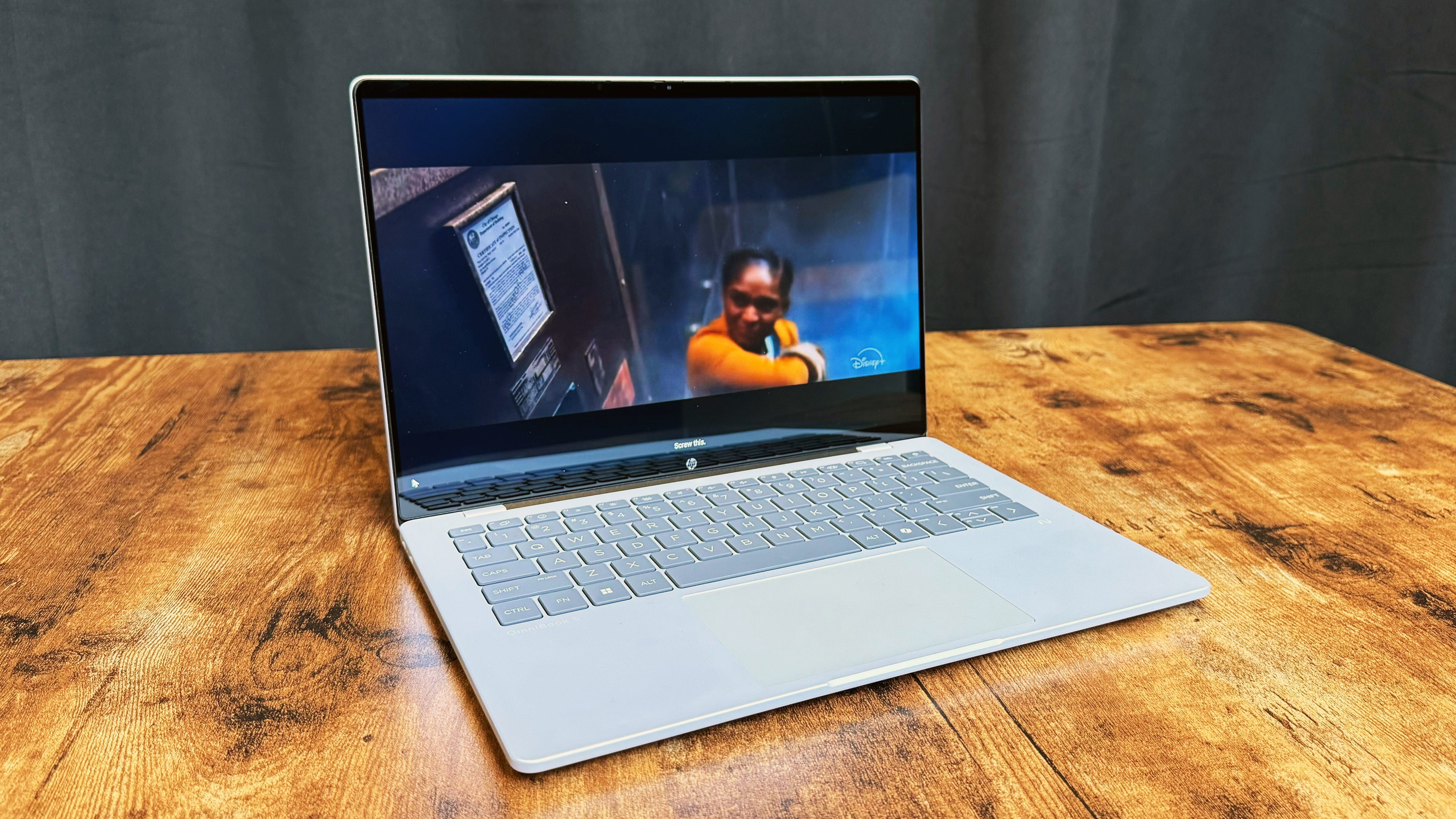 HP Omnibook 5 14 AI PC روی یک میز چوبی در برابر پس زمینه سیاه.