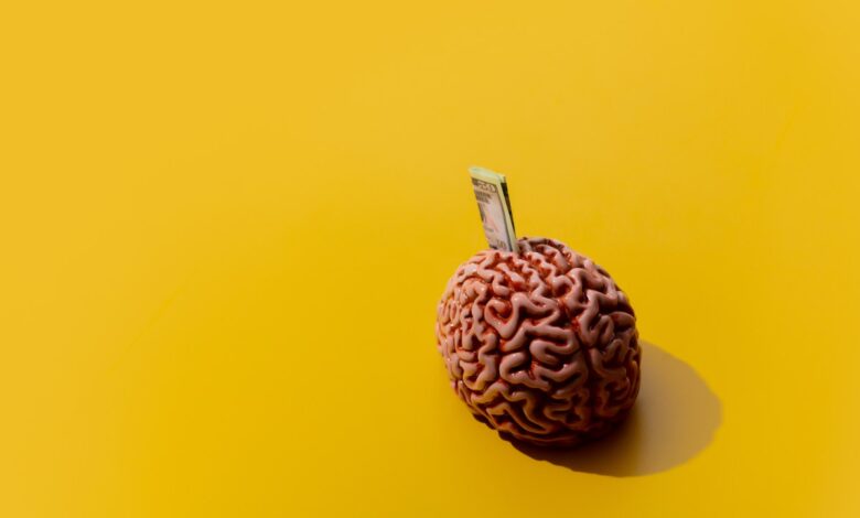Image of money sticking out of a brain against a yellow background