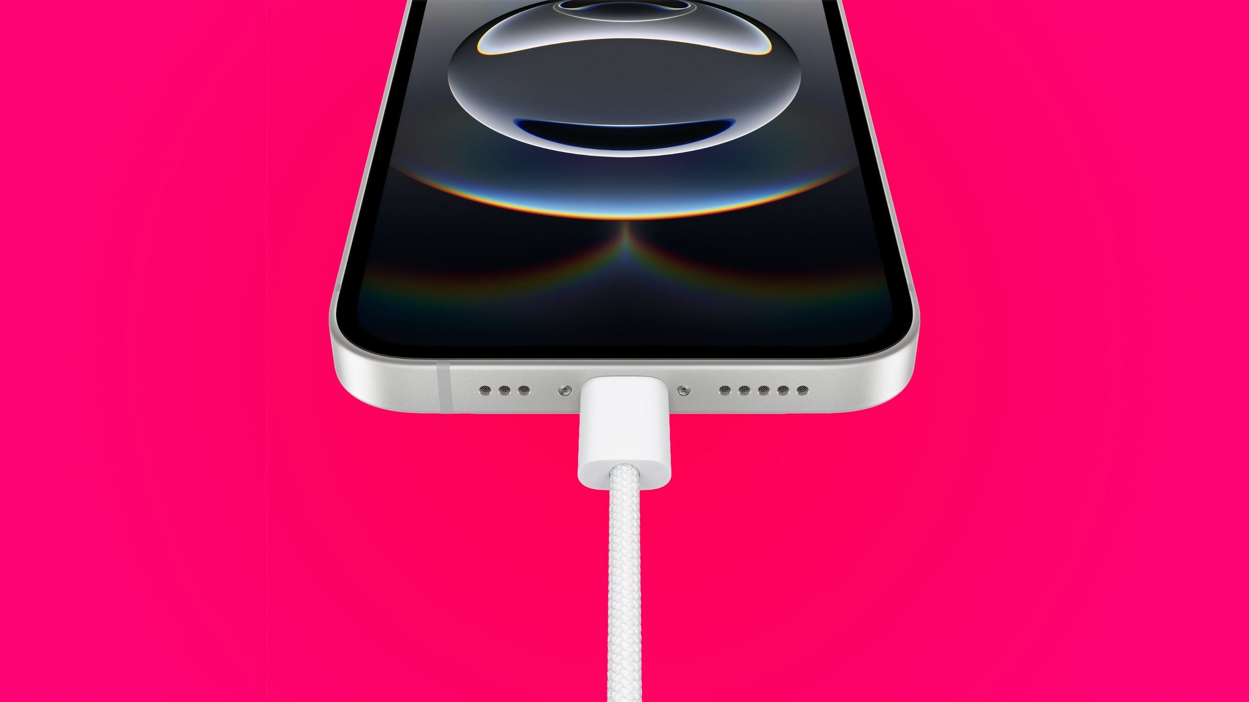 یک آیفون 16E سفید در مورد USB-C در پس زمینه شیب قرمز شارژ می شود.