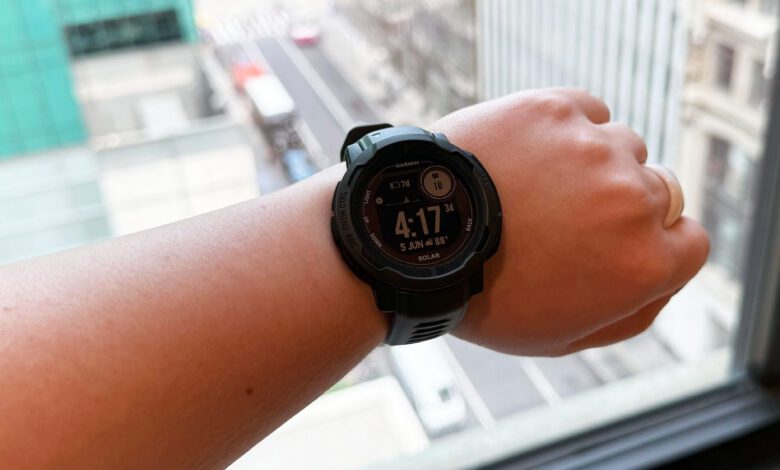 Garmin Instinct 2 Solar on left wrist, in front of a window overlooking Bryant Park in New York City.