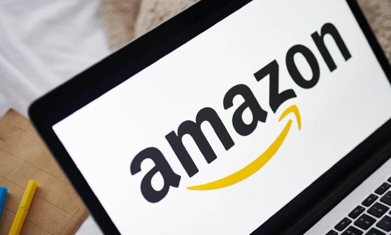 Amazon logo on laptop next to blue and yellow pens.