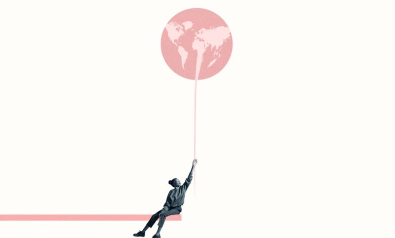 Young woman holding at large pink balloon with world map while sitting on ramp against white background