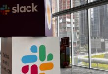 Cubes with Slack name and logo stacked on one another with city view in background.