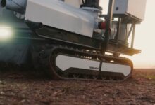 An autonomous, tracked robot sits on a dirt patch.
